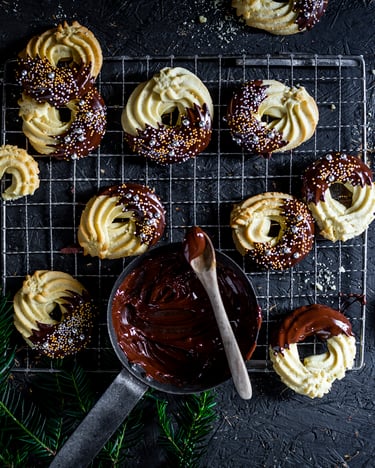 Klassisches Spritzgebaeck mit Schokoguss und Streuseln auf einem Abtropfgitter und dunklem Untergrund