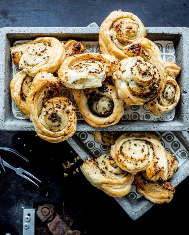 Knoblauchteigschnecken mit Thymian in eckigen Schälchen mit kleinen Gäbelchen auf schwarzem Untergrund.