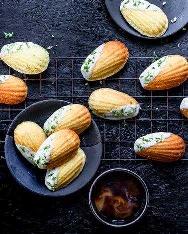 Goldgelbe Limetten-Madeleines mit weißer Schokoladenglasur auf einem dunklen Hintergrund.
