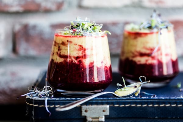 Zwei kleine Gläser mit rot-gelb geschichtetem Smoothie mit Senfkresse auf Koffer vor Ziegelwand