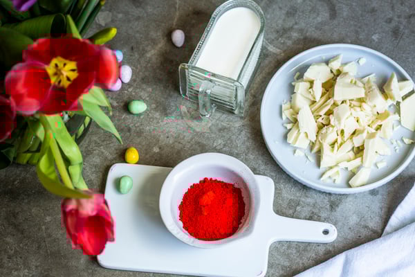 Schale mit Sahne, Teller mit gehackter weißer Schokolade und Schälchen mit roter Lebensmittelfarbe in Pulverform