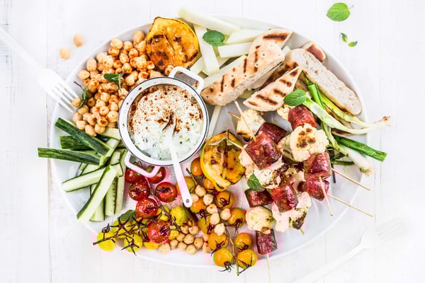Salatplatte mit viel Gemüse, Brot und Chorizo auf weißem Untergrund mit einer Gabel