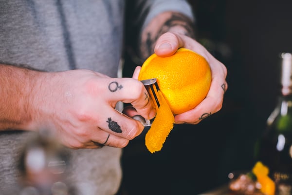 Mit einem Sparschäler wird eine Zeste von einer Orange geschnitten.