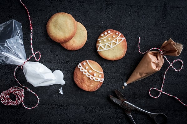Alternative Spritztüten gebastelt aus einem Gefrierbeutel und Backpapier neben Keksen mit Zuckerguss auf dunklem Untergrund