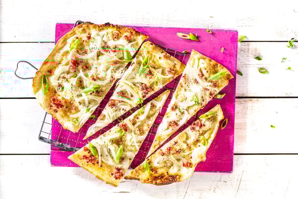 Flammkuchen mit Zwiebeln und Speck in Stücke geschnitten auf einem pinken Brett.