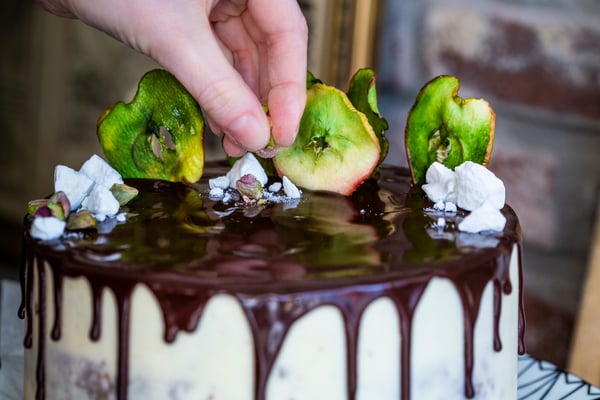 Grüne Apfelchips, gebrochener weißer Schaumzucker und Pistazien als Deko auf einem Drip Cake