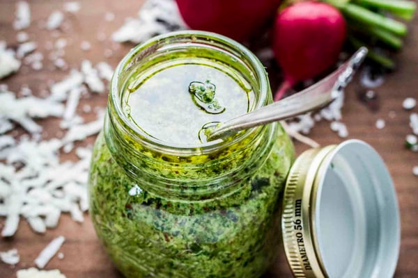 Radieschenblätter-Pesto im Glas mit Schraubdeckel neben Parmesanhobeln.