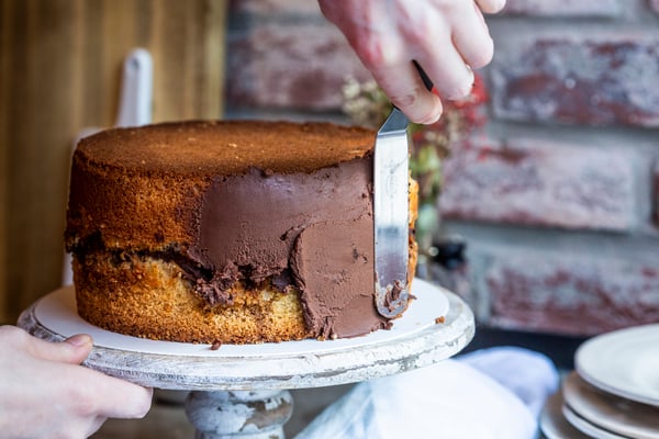 Torte wird mithilfe einer Palette mit einer dunklen Schokoladenganache eingestrichen.