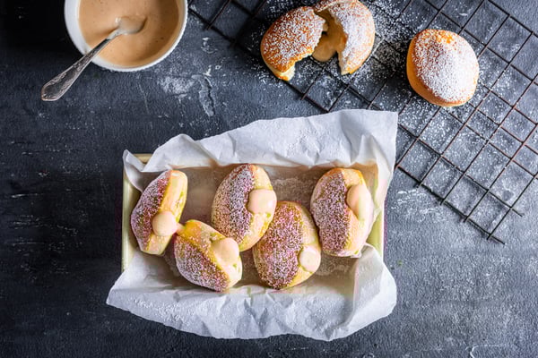 Bomboloni mit Crema pasticcera in einem Korb, der mit Backpapier ausgelegt ist.
