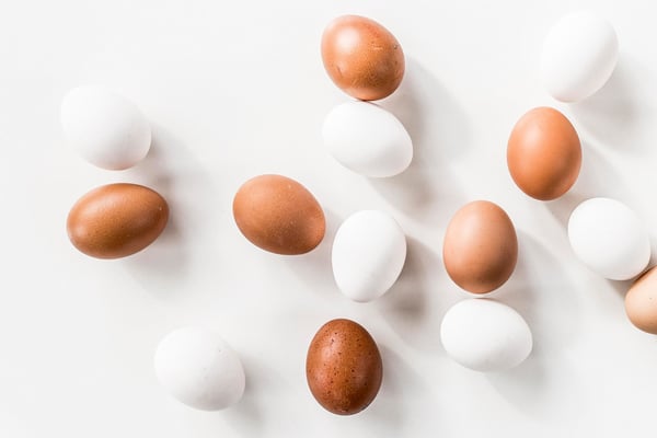 weiße und braune Eier auf weißem Untergrund von oben fotografiert