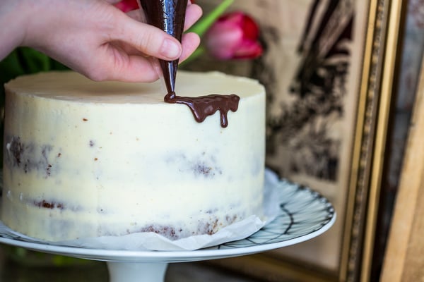 Ein heller Naked Cake wird mit einer dunklen Schokoladenganache aus einem Spritzbeutel dekoriert