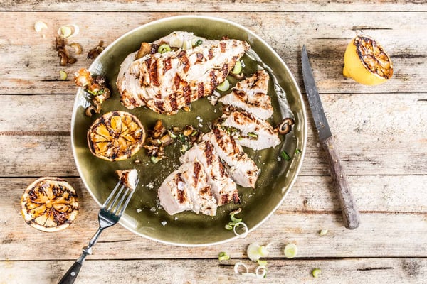 Aufgeschnittenes gegrilltes Hähnchenbrustfiletmi Knoblauch und Zitrone auf einem Teller serviert mit Besteck