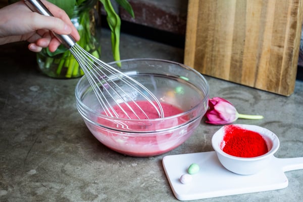Rote Lebensmittelfarbe, Sahne und weiße Kuvertüre werden in einer Schale zu einer rosa Ganache verrührt.