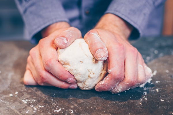 Teig der Pizza Margherita wird auf Arbeitsfläche von Hand durchgeknetet