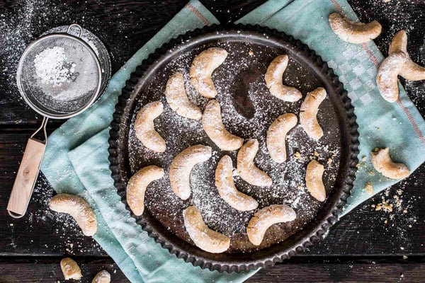 Vanillekipferl mit Puderzucker auf einer Tarteform serviert und einer mintfarbener Stoffserviette.